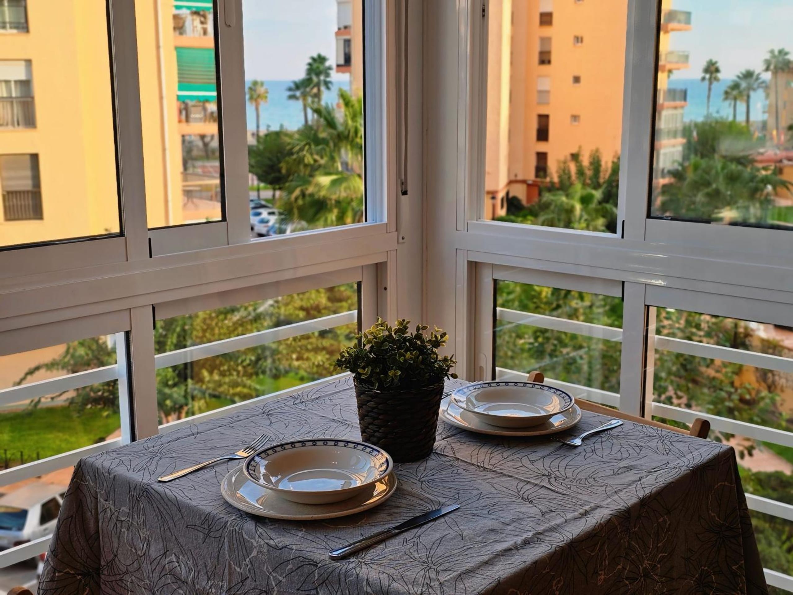 Mesa preparada junto a ventana con vistas al mar y edificios.